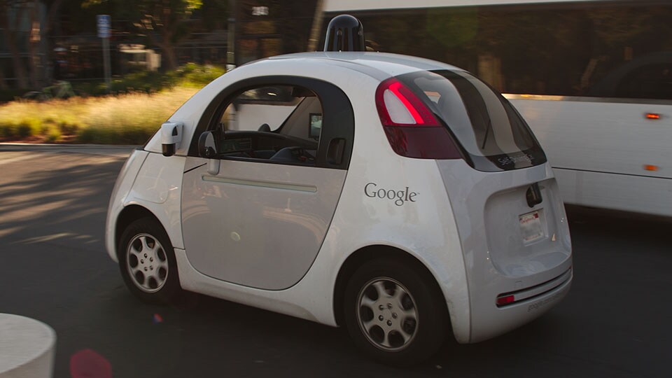 A Google self driving car drives past a double-deck commuter bus at Google's headquarters in Mountain View, CA, USA