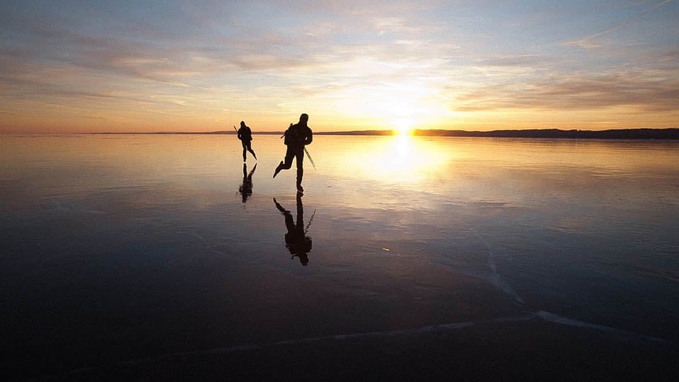 Two people ice skating across natural lakes in Sweden