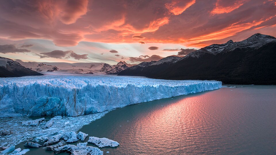 A stunning view of snow-capped mountains, glaciers and an orange sky in Patagonia